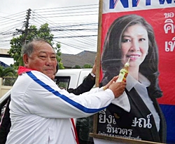 Out campaigning on a hot day, Pheu Thai candidate Adm. Surapol Chandang jokingly offers a cool drink to Prime Minister candidate Yinglak Shinawatra’s poster.